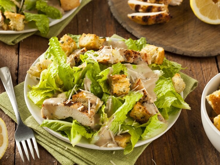 Caesar Salad mit gegrillter Putenbrust und Salatblättern / runder Teller / Gabel / Stoffserviette / angeschnittene Zitrone / Draufsicht, schräg
