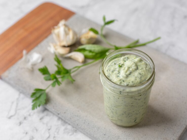 Ein Schraubglas mit einem grünen Dip auf einem Holzbrett.