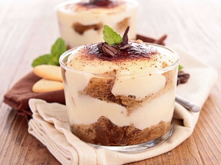 Zwei Gläser mit Biscoff-Tiramisu, bestreut mit Kakaopulver und Kaffeebohnen, geschichtet mit Karamellkeksen.