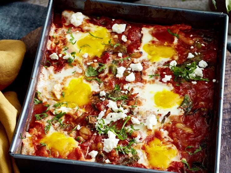 In einer Auflaufform ist ein Ofen-Shakshuka mit Spinat angerichtet. Es ist mit Petersilie bestreut. 