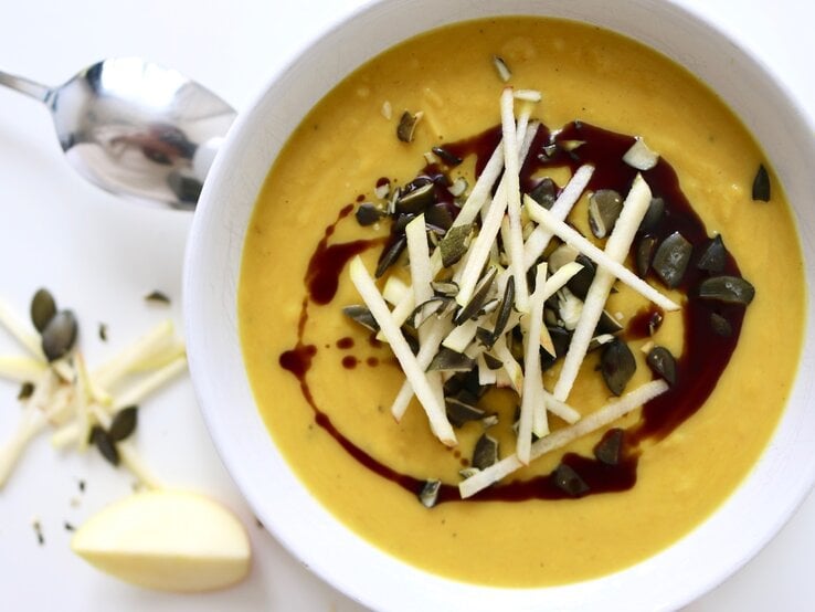 Kürbis-Apfel-Suppe mit Curry in einer Schüssel, dekoriert mit Samen und Kernen, von oben fotografiert.