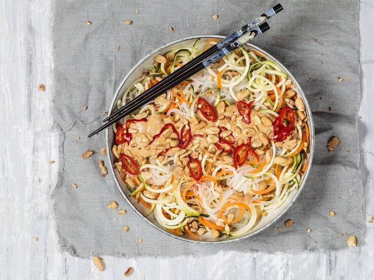 Veganer Glasnudelsalat mit leckerer Erdnusssoße auf einem grauen Tuch. Dazu Stäbchen. 
