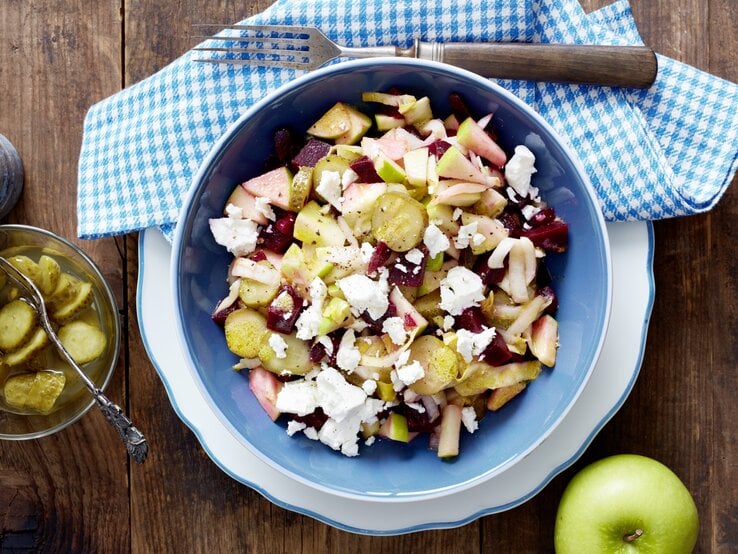 Rote-Bete-Salat mit Schafskäse, Apfelstücken und sauren Gurken, serviert in einer großen Schale auf einem Küchentuch. 
