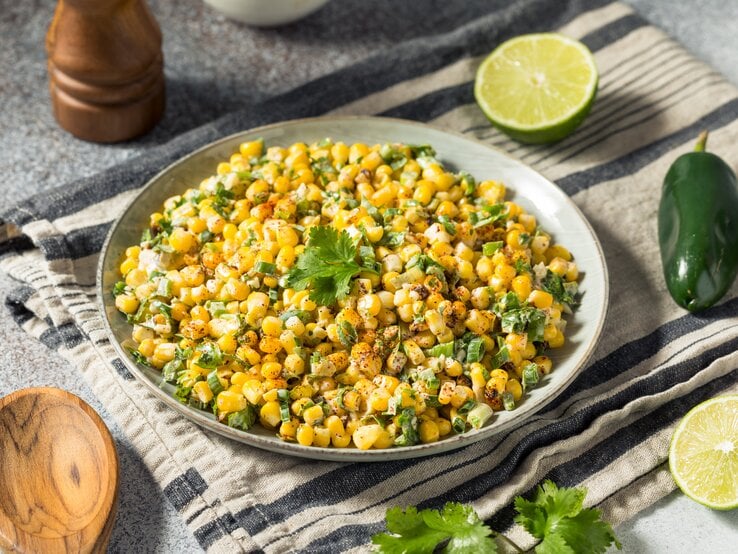 Ein grauer tiefer Teller gefüllt mit mexikanischem Maissalat auf einem gestreiften Küchentuch