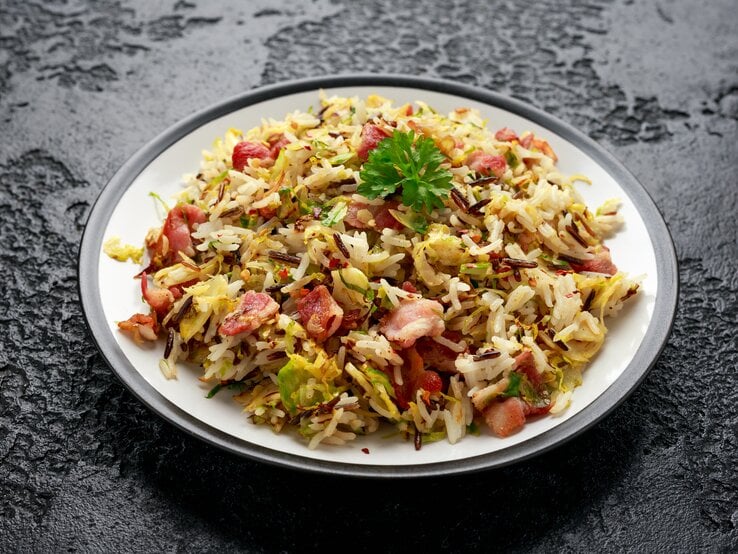 Ein Teller mit Rosenkohl-Bratreis mit Speck auf einem dunklen Untergrund.