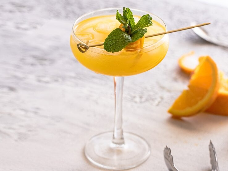 Ein Coupette-Glas mit dem gelben Drink auf einem grauen Holztisch.