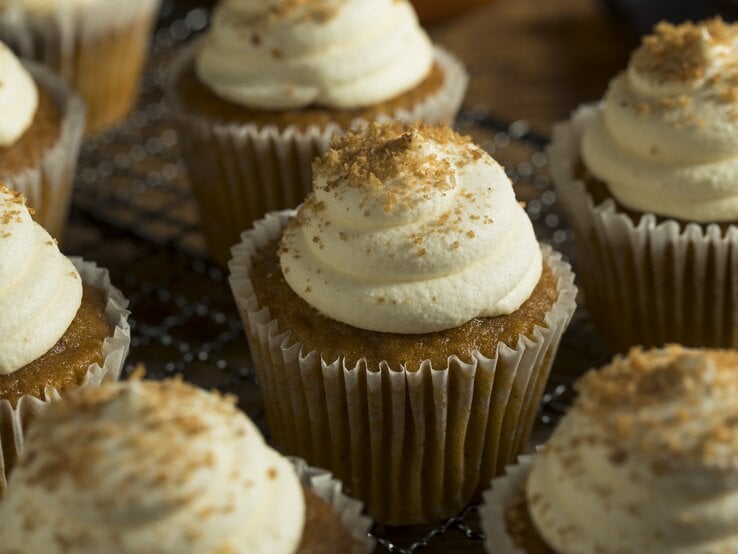 Ein paar Zimtschnecken-Cupcakes mit Creme-Haube auf einem Holzbrett.
