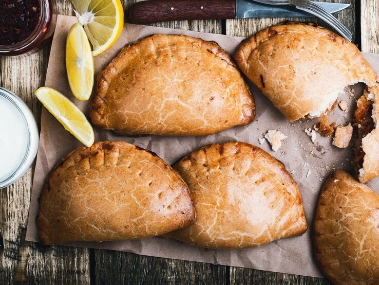 Empanadas nach mexikanischer Art auf einem Backpapier. Daneben Zitronen. 