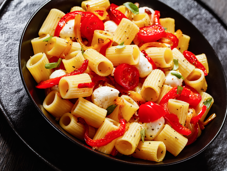 Paprika-Nudelsalat mit Pfeffer auf schwarzem Teller. 