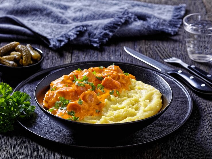 Finnischer Würstchen-Eintopf Nakkikastike mit Kartoffelpüree in schwarzer Schüssel.