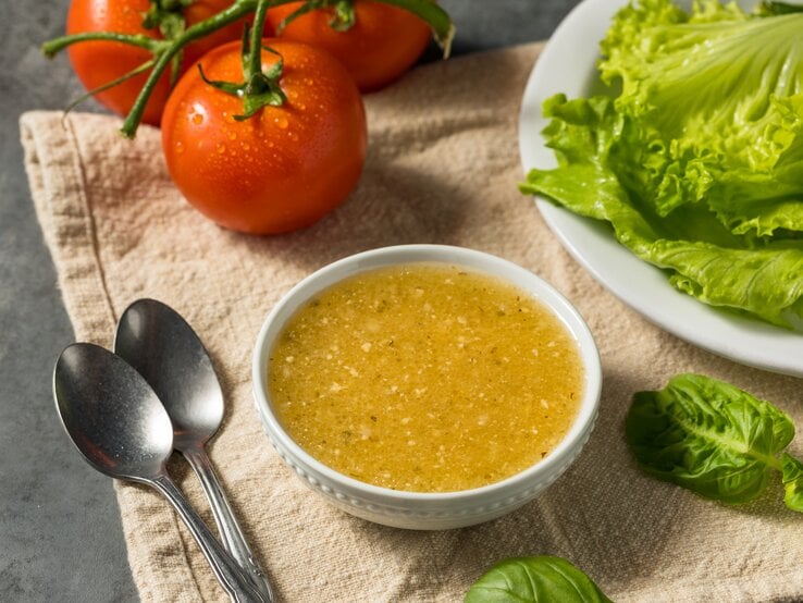 italienisches Knoblauchdressing in kleiner Schale. Daneben Tomaten und Blattsalat.  | © Getty Images/bhofack2