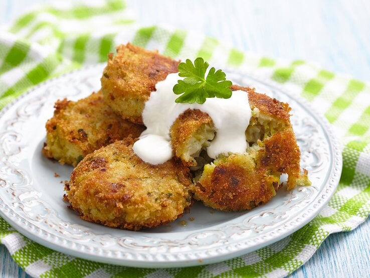Ein weißer flacher Teller mit vier Rosenkohl-Bratlingen darauf. Alles auf einer grün-weiß-karierten Tischdecke und Holztisch fotografiert.