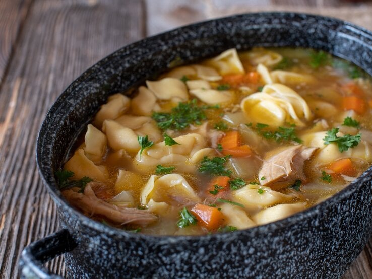 Ein Topf mit Tortellini-Hühnersuppe auf einem Holztisch.