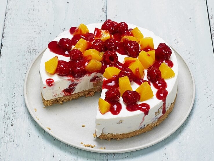 Auf einem Teller liegt ein Pfirsich-Melba-Käsekuchen. Er ist mit Himbeersoße überzogen. 