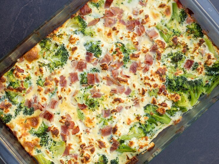 Gläserne Auflaufform gefüllt mit übebackenem Brokkoli-Schinken-Gratin auf dunklem Untergrund.  | © Shutterstock / Samuel Cohen