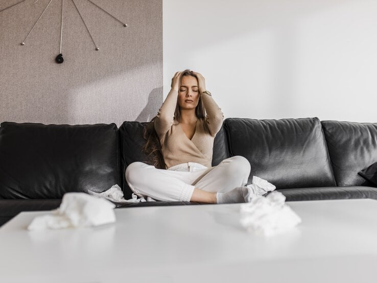 Frau sitzt mit Händen am Kopf auf Sofa