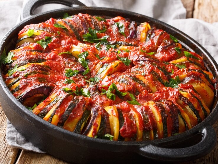 Ofenfrisches Briam im Gusstopf auf Holzunterlage mit Küchenhandtuch