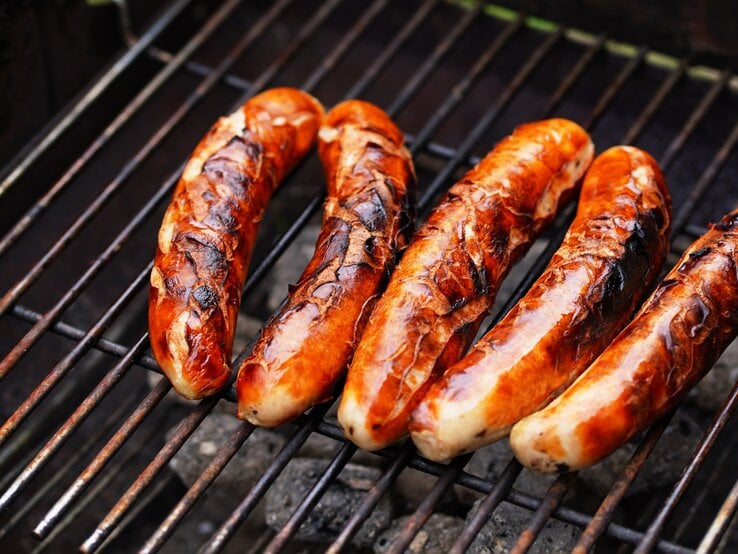 Draufsicht: Fünf Thüringer Rostbratwürste liegen auf einem Holzkohlegroll.