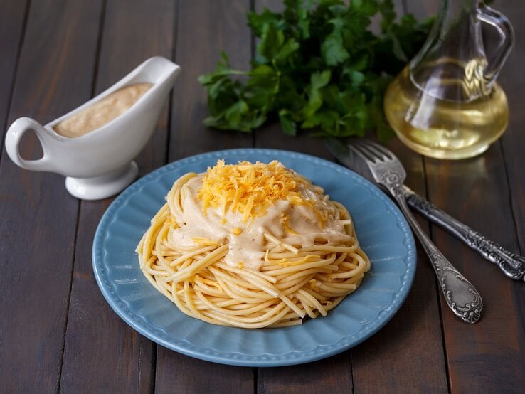 EIn Teller mit Pasta mit Schmelzkäse-Zitronensoße auf einem Holztisch.