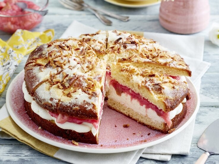 Auf einem Teller ist ein gefüllter Rhabarber-Butterkuchen angerichtet. Er ist mit Puderzucker bestreut.