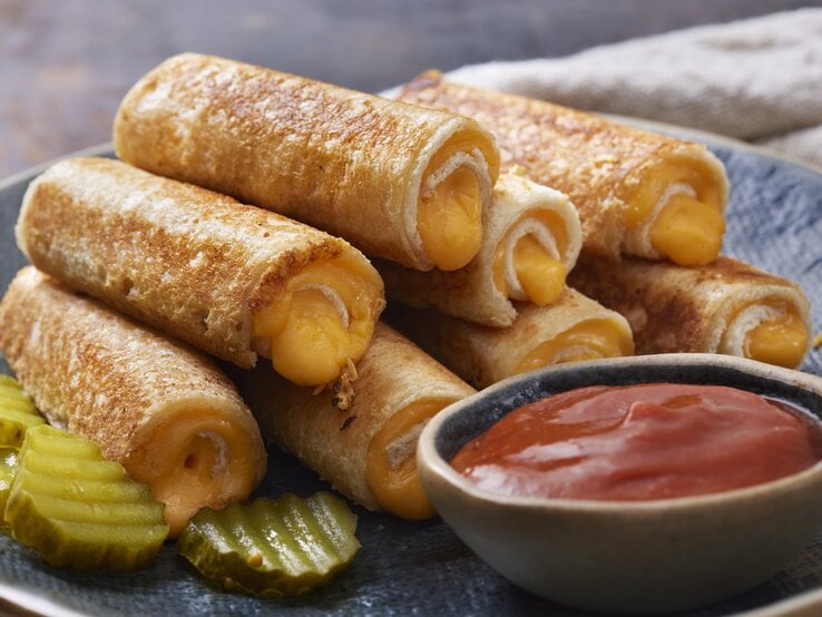 Gerollte Toastbrote mit Käse gefüllt zu Salsa auf dunklem Teller. | © Getty Images/LauriPatterson