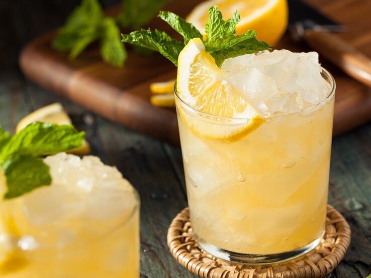 Ein Glas mit dem Dry Limoni auf einem Holztisch mit Zitrone und Minze.