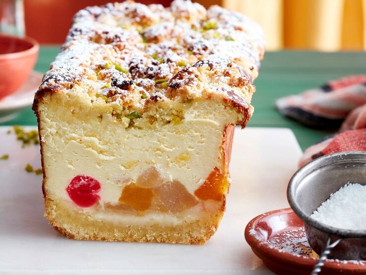 Auf einem Brett steht ein Tutti-Frutti-Käsekuchen aus der Kastenform. Er ist mit Puderzucker bestreut. | © EAT CLUB / Isabell Triemer