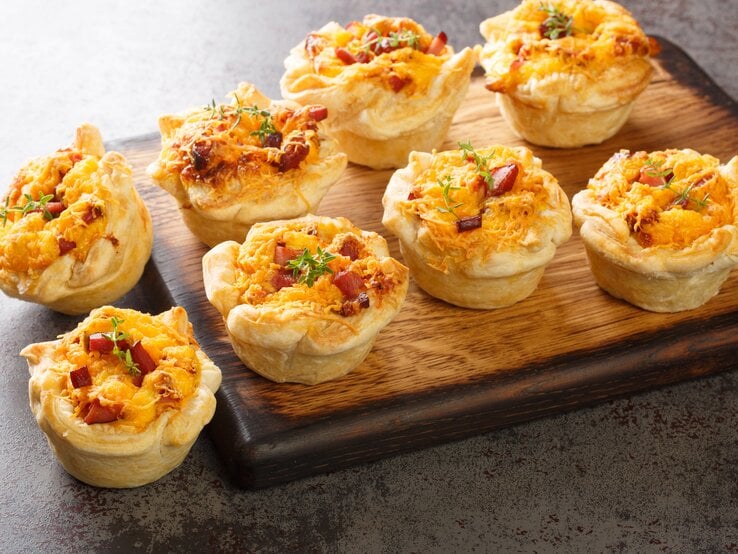 Blätterteig-Muffins mit Schinken & Käse auf Holzbrett.  | © Getty Images/ALLEKO