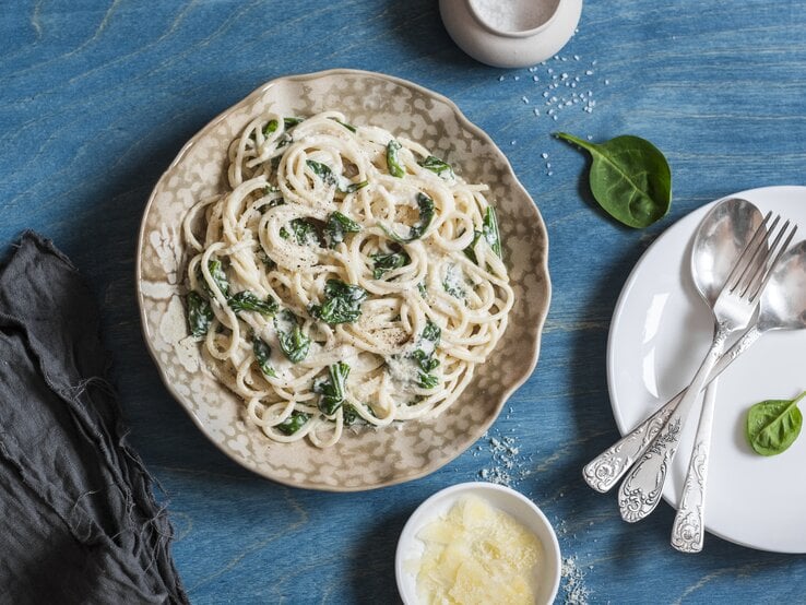 Spaghetti in Spinat-Schmand-Soße auf gewelltem Teller auf blauem Untergrund. 