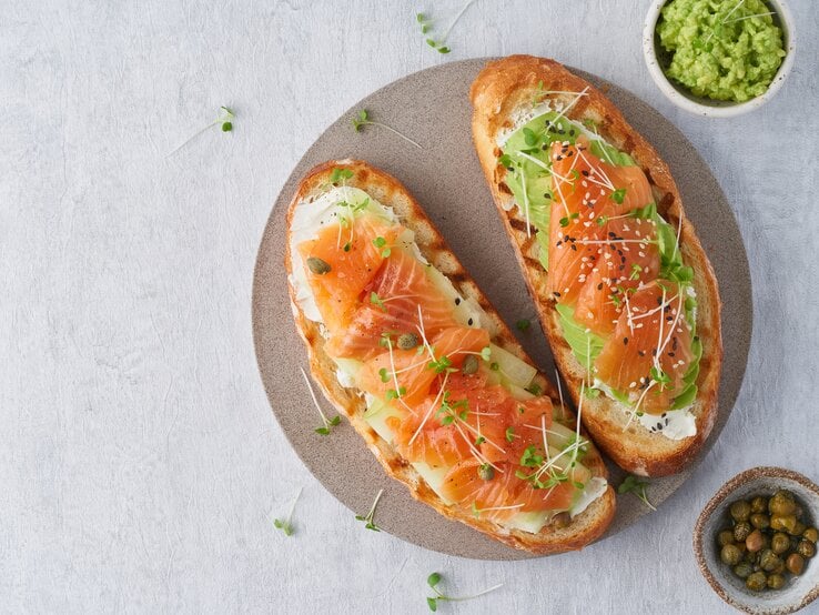Draufsicht: Ein Teller auf dem zwei Low-Carb-Toast mit Lachs liegen. Daneben ist ein rundes Gefäß mit Avocadocreme und eines mit Kapern. | © Shutterstock / Nata Bene