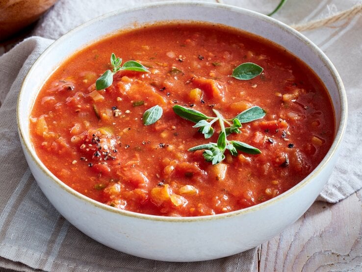 In einer Schüssel ist eine Portion feurige Tomatensuppe mit Rosmarin angerichtet. Sie ist mit Basilikum verfeinert.