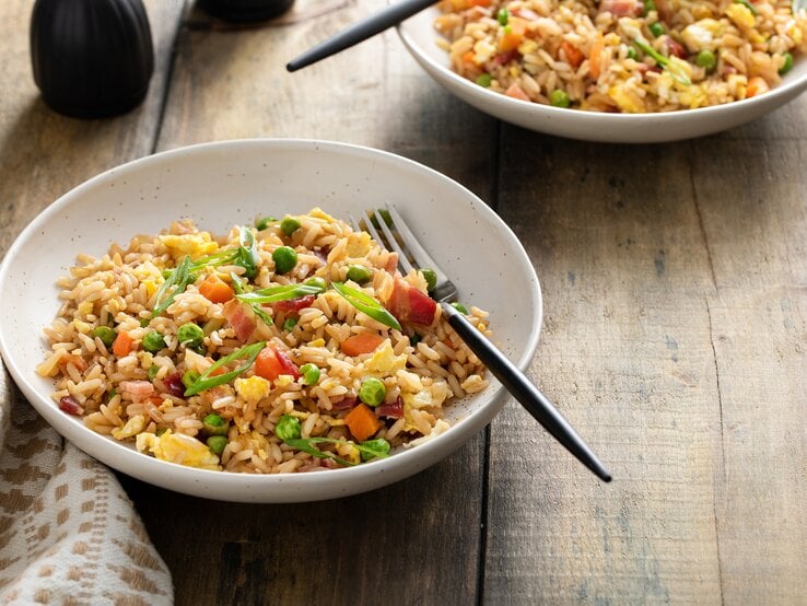 Zwei Schüsseln mit gebratenen Frühstücksreis mit Ei & Speck stehen auf einem hölzernen Untergrund.