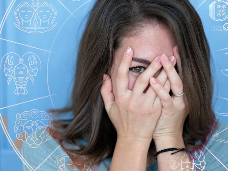 Frau schämt sich und versteckt sich hinter Händen mit Sternkreissymbolen