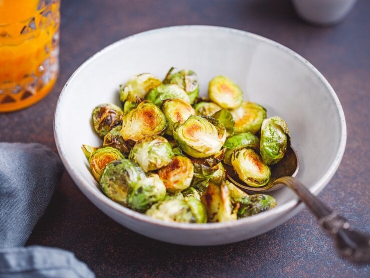 Eine Schüssel halbierter gebackener Rosenkohl mit Sojasoße, darin ein Löffel.