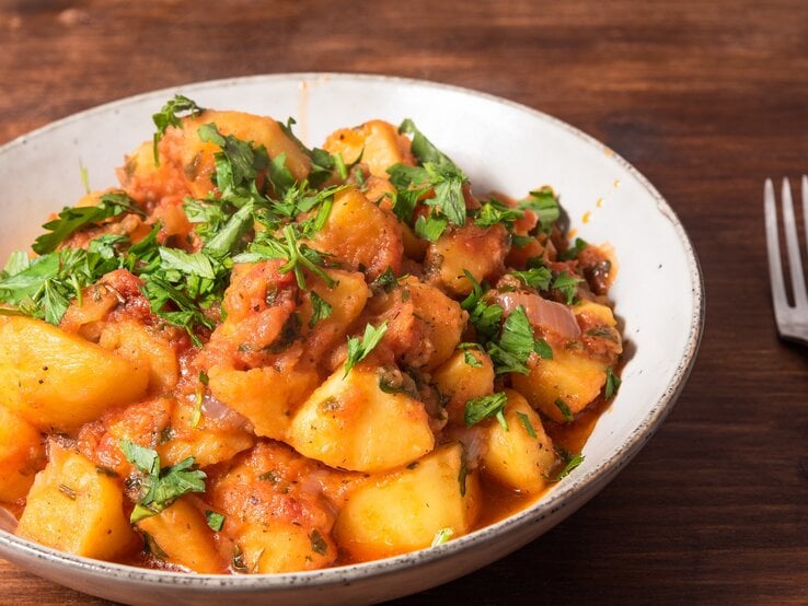 Kartoffelsalat mit Harissa-Dressing und Petersilie in einer Schüssel, daneben eine Gabel.