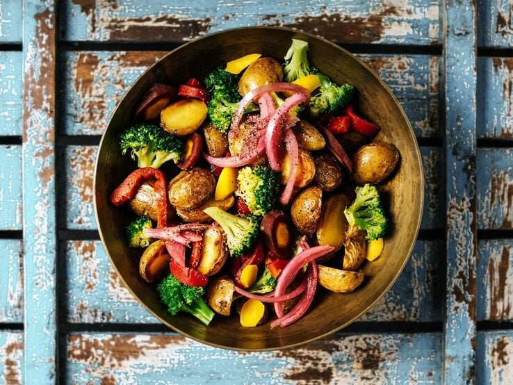 Gegrillter Kartoffelsalat mit Gemüse, Hirtenkäse und rotem Pesto in Schale auf blauem Holz. Aufnahme aus der Vogelperspektive.