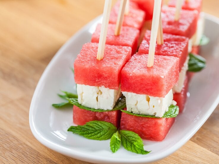 Wassermelonen-Feta-Spieße auf weißem Teller, angerichtet auf hölzernem Untergrund.  | © Getty Images/ermandogan