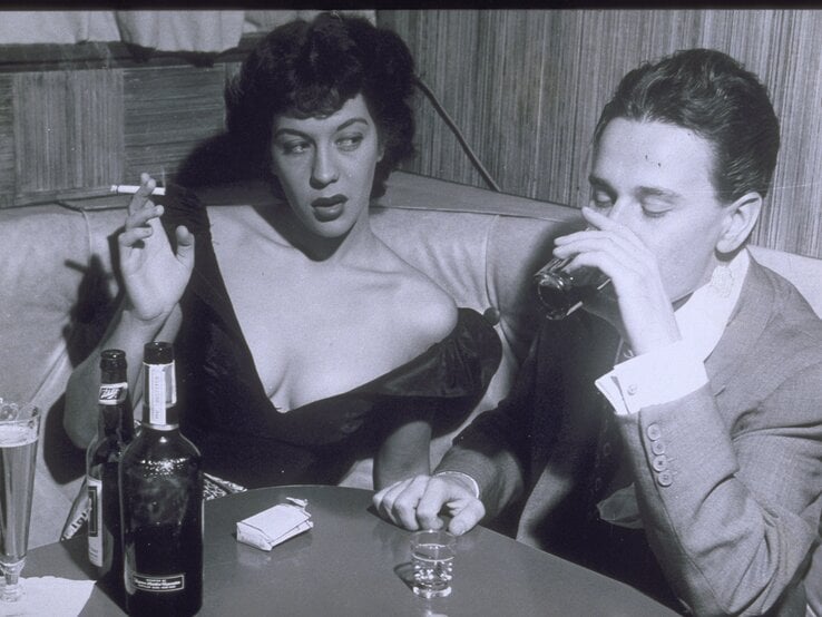 Ein Mann und eine Frau sitzen am Ecktisch einer Bar und trinken und rauchen.