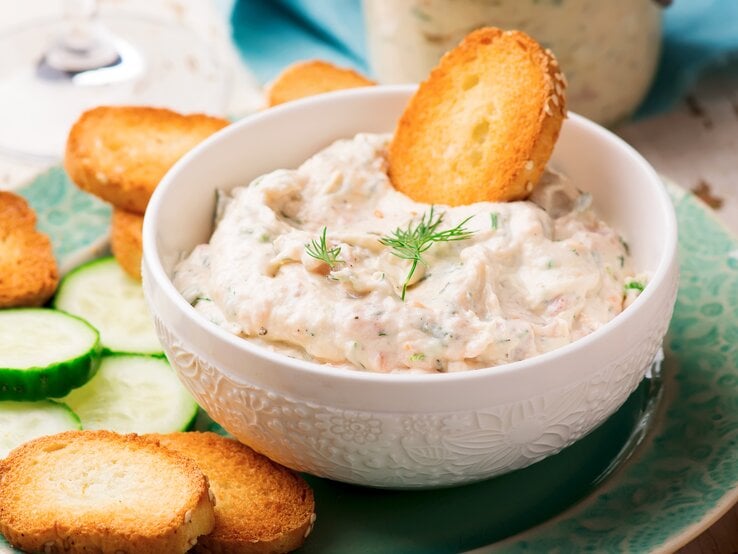 Lachscreme mit Frischkäse in weißer Schüssel mit Brotchips auf blauem Teller. 