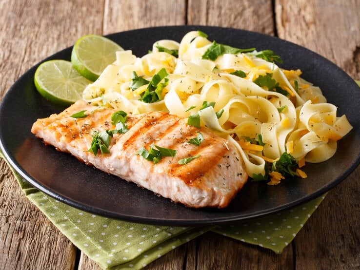 Ein schwarzer Teller mit Pasta mit Lachs und Cheddar auf einem rustikalen Holztisch.