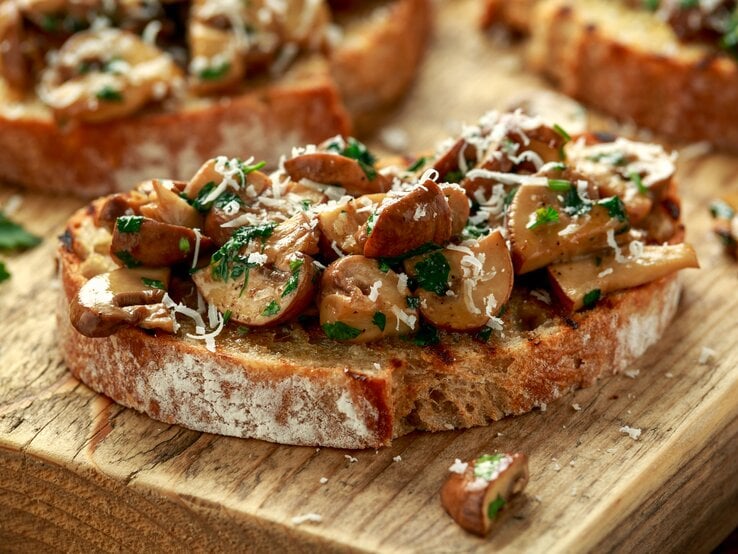 Eine Pilzstulle mit Knoblauchfrischkäse und Parmesan auf einem Holzbrett.