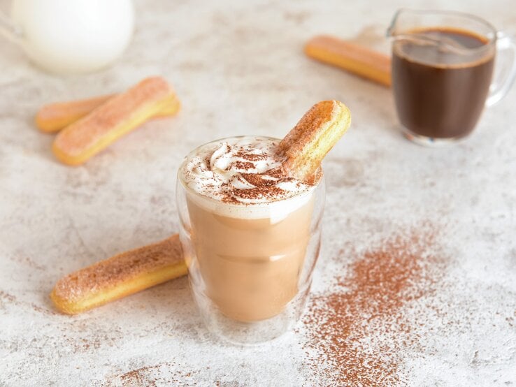 Ein Glas mit Tiramisu-Latte neben einem Löffelbiskuit.