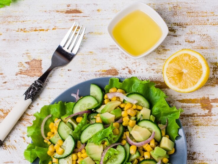Schale mit Mango-Dressing neben einem Teller Salat mit Gurke und Mais auf hölzernem Untergrund.  | © Getty Images/zia_shusha
