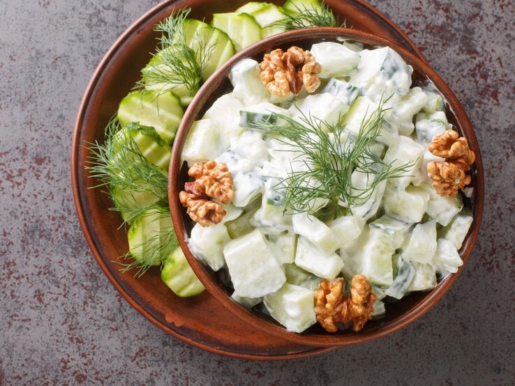 Bulgarischer Gurkensalat mit frischem Dill, Joghurt und ganzen Walnüssen, serviert in einer dunklen Keramikschale auf steinernem Untergrund. 