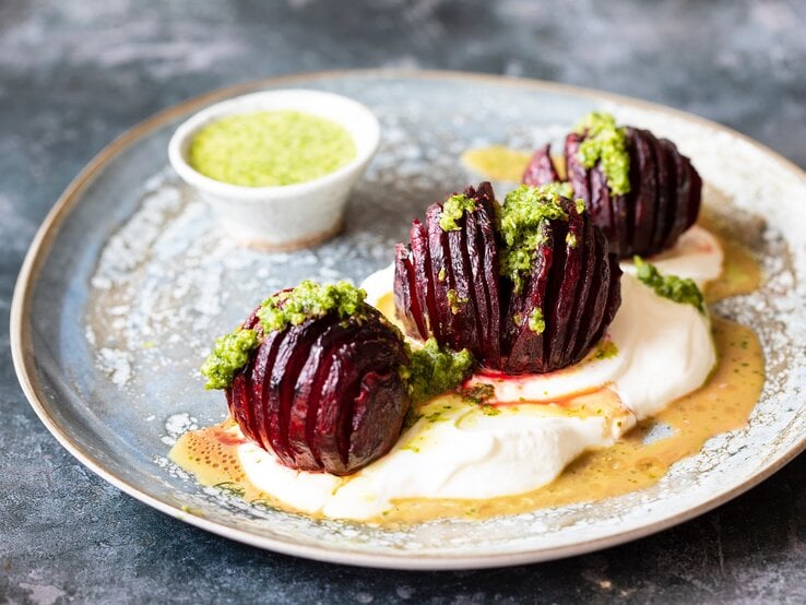 Ein Teller mit drei Hasselback-Beten, grünem Dressing und Joghurt.