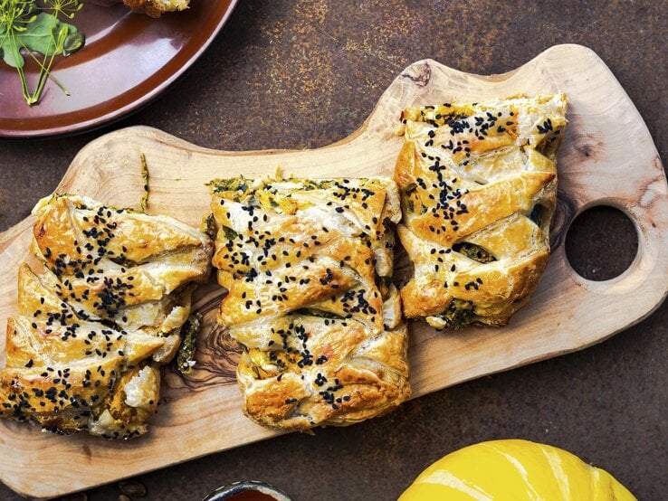 Auf einem Schneidebrett liegt Blätterteiggebäck gefüllt mit Kürbis, Spinat und Feta. Es ist mit Sesam bestreut. | © StockFood / Thorpe, Lara Jane