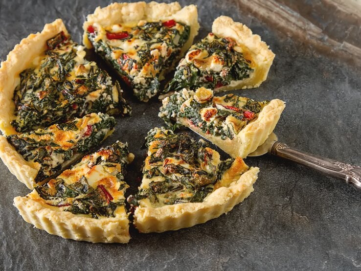 Eine geschnittene vegane Mangold-Quiche mit Lauch auf dunklem Untergrund.