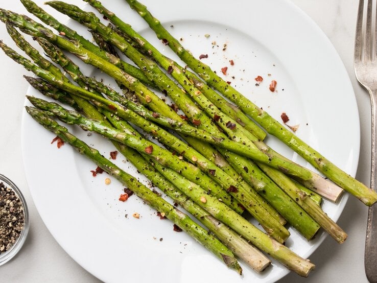 Ein Teller mit Knoblauch-Zitronen-Spargel. daneben eine Gabel, alles Draufsicht.
