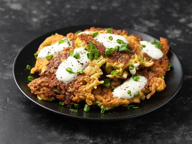 Ein schwarzer Teller mt Kohl-Pfannkuchen auf einem dunklen Tisch.