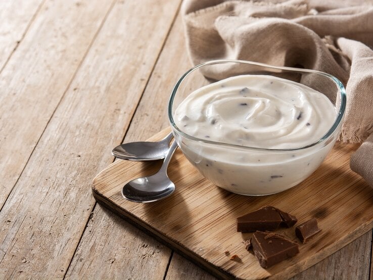Ein Glas Herrencreme auf einem Holzbrett neben zwei Löffeln.